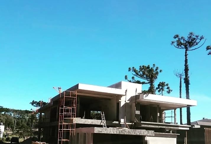 Residência em construção, com andaimes e araucárias ao fundo